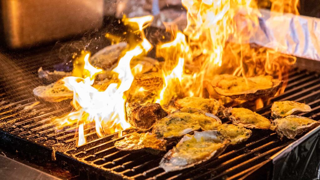 Oysters on the menu being cooked with fire on a grill